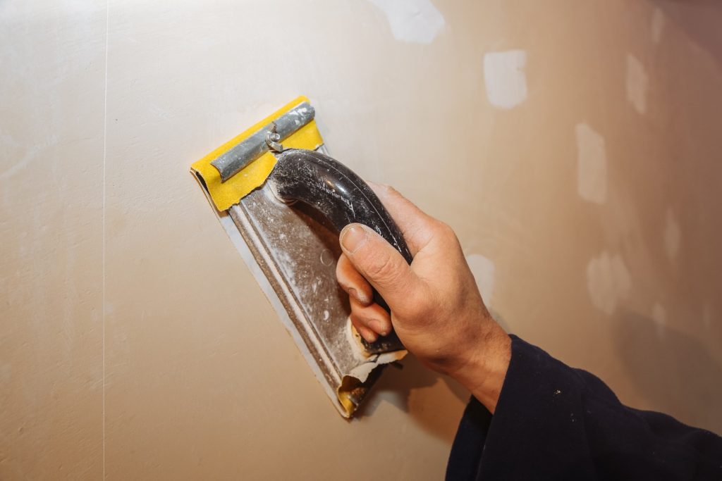 Drywall contractor smoothing joint compound on drywall surface.
